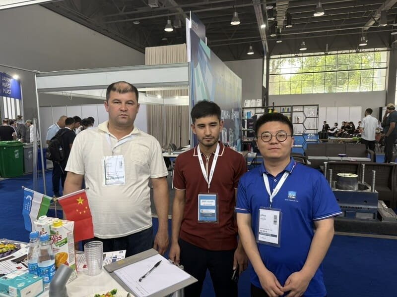 Three business visitors standing in front of HVACore company logo wall with Chinese lantern decorations visible above